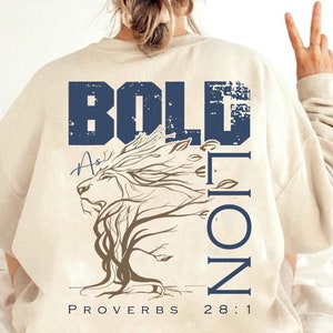 May include: A beige sweatshirt with a blue and white graphic print of a lion with the words "BOLD AS A LION" and "PROVERBS 28:1".