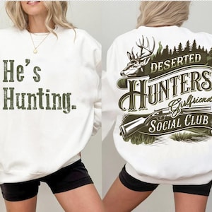 May include: White sweatshirt with the text "He's Hunting." on the front and a green and brown graphic on the back that says "Deserted Hunters Girlfriends Social Club" with a deer and a rifle.