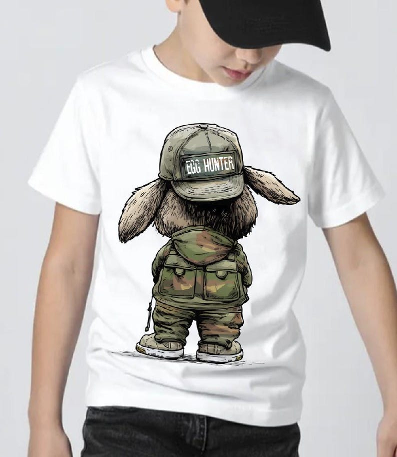 Puede incluir: Camiseta blanca con una ilustraci&oacute;n de dibujos animados de un conejo. El conejo lleva un atuendo de estilo militar y una gorra con la inscripci&oacute;n "EGG HUNTER". La imagen muestra al conejo por detr&aacute;s, con sus orejas y los detalles de su atuendo. La camiseta la lleva una persona.