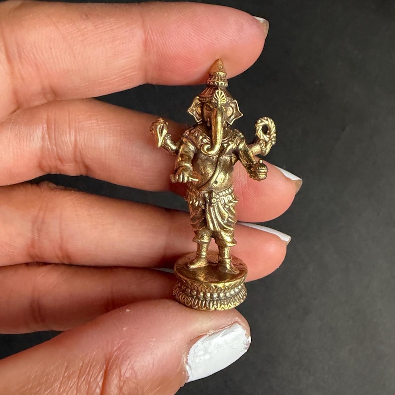 May include: A small, detailed brass statue of the Hindu deity Ganesha. The statue features intricate carvings, an elephant head, and multiple arms. It stands on a decorative base, showcasing traditional Indian artistry.