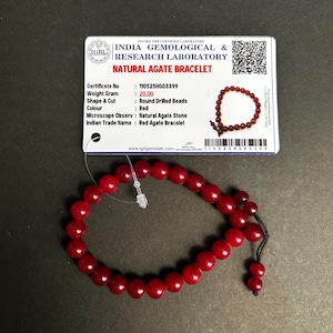 May include: A red natural agate bracelet with round drilled beads. The bracelet is displayed with a certificate from the India Gemological & Research Laboratory. The certificate states the weight is 20.00 grams.