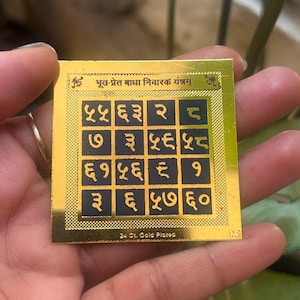 May include: A gold-plated square with a grid of black squares containing numbers and symbols. The top of the square has text in a foreign language. The bottom of the square has the text "24 Ct. Gold Plated".