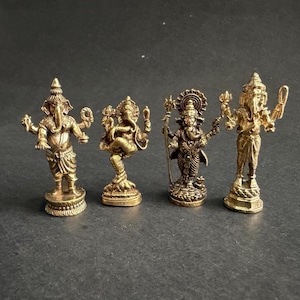 May include: Four small, detailed brass statues of Hindu deities. The statues depict various forms of Ganesha and other figures, each with unique poses and attributes. The statues are on a dark surface.