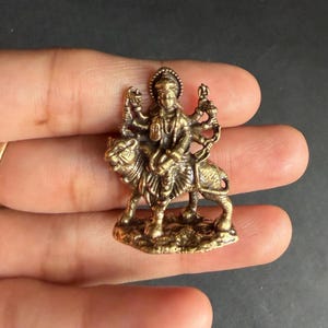 Peut inclure: Petite figurine en laiton détaillée représentant une divinité chevauchant un tigre. La figure à plusieurs bras est ornée de bijoux complexes et d'un halo. Le tigre est représenté dans une pose dynamique, ajoutant au sentiment général de mouvement et de puissance. C'est un objet religieux ou spirituel.