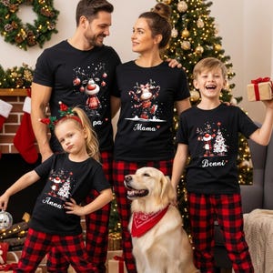 Könnte beinhalten: Eine Familie trägt passende schwarze Weihnachtsshirts und rot karierte Schlafanzughosen. Die Shirts zeigen Rentier- und Weihnachtsbaumdesigns mit Namen. Ein Golden Retriever trägt ein rotes Halstuch. Ein Weihnachtsbaum und ein Kamin befinden sich im Hintergrund.