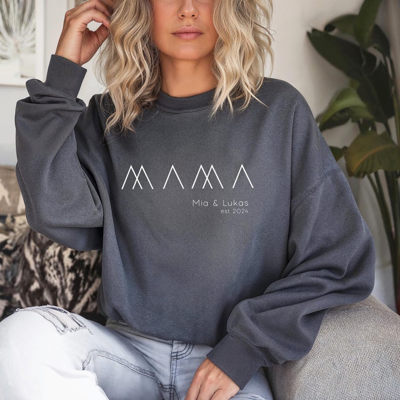 May include: A dark gray sweatshirt with a white graphic of three mountain peaks and the text "MAMA" above the text "Mia & Lukas est 2024".