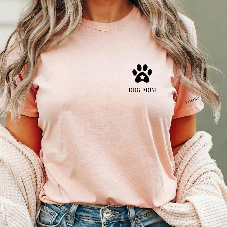 May include: A pink t-shirt with a black paw print and a star in the center. The text "DOG MOM" is printed below the paw print.