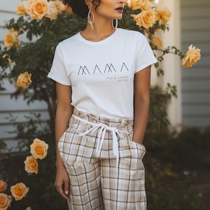 May include: White t-shirt with a black graphic of the word "MAMA" with three triangles. The text "Mia & Lukas est. 2024" is below the graphic.