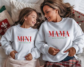 May include: White Christmas themed sweatshirts for a mother and child. The mother's sweatshirt says "Mama Louise Noah merry Christmas" and the child's sweatshirt says "Mini Louise Noah merry Christmas".