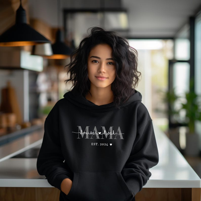 Może przedstawiać: Czarna bluza z kapturem z napisem "MAMA" i grafiką bicia serca z napisem "double the love" nad nim. Napis "EST. 2024" znajduje się pod grafiką.