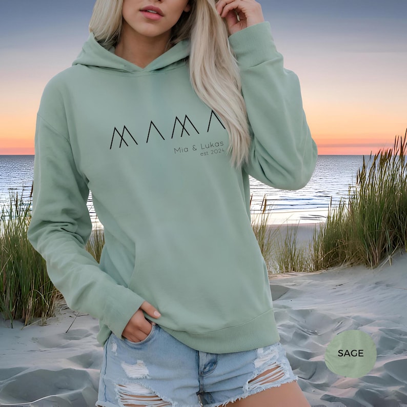 May include: Sage green hooded sweatshirt with the text "MAMA" in black stylized mountain shapes and the text "Mia & Lukas est. 2014" below.