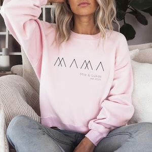 May include: Pink sweatshirt with the word "MAMA" in black stylized letters, with the text "Mia & Lukas est 2024" below.