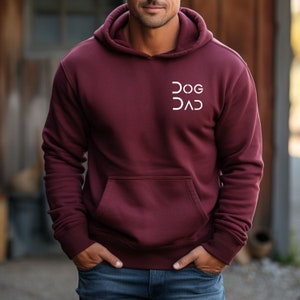 Pu&ograve; includere: Una felpa con cappuccio color bordeaux con una grafica bianca che dice "DOG DAD" sul davanti.