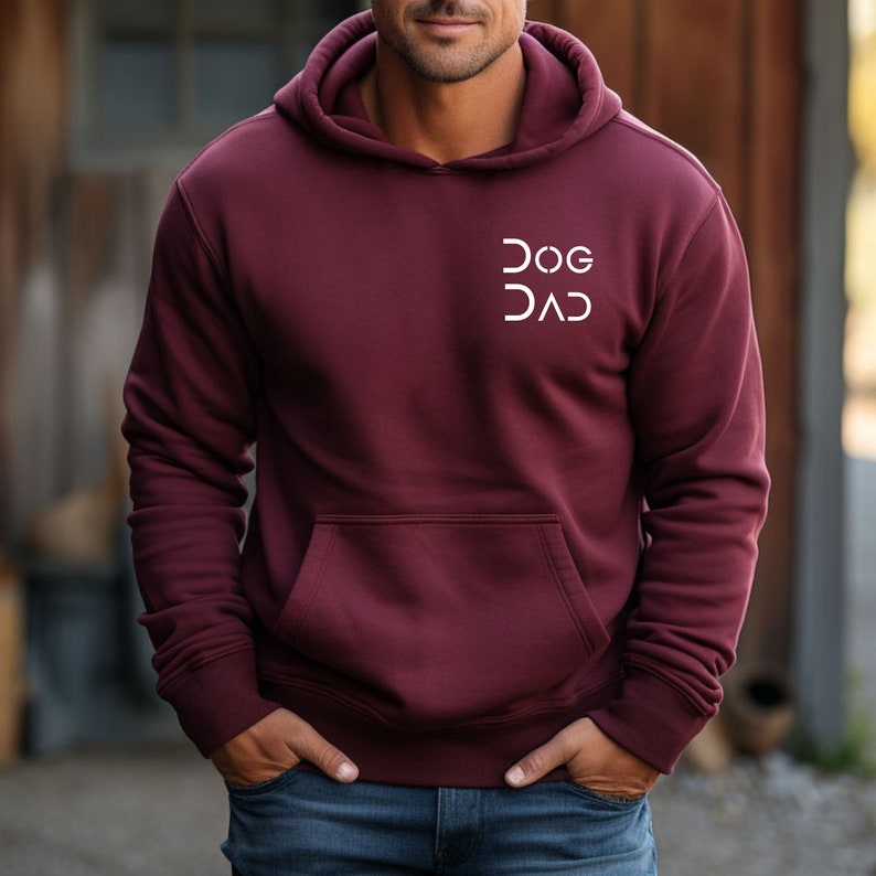 Pu&ograve; includere: Una felpa con cappuccio color bordeaux con una grafica bianca che dice "DOG DAD" sul davanti.