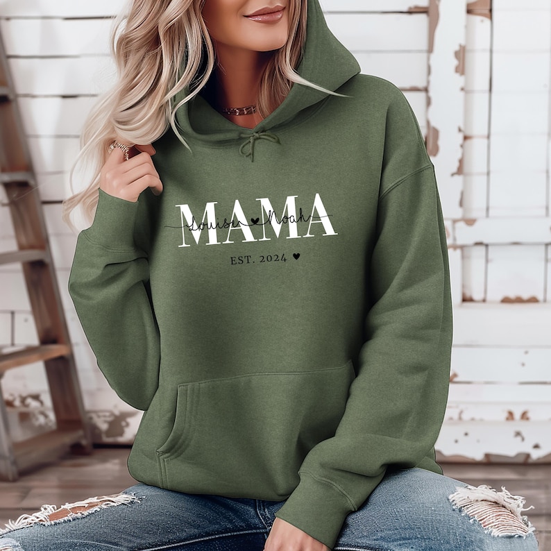 Może przedstawiać: Zielona bluza z kapturem z napisem "MAMA" w białych literach. Pod napisem "MAMA" znajduje się napis "Louise & Noah" mniejszą czcionką, z sercem między imionami. Pod imionami znajduje się napis "EST. 2024" z sercem.