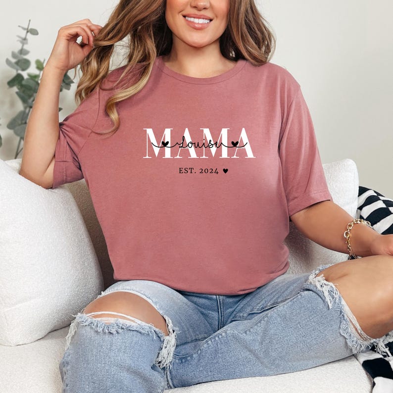 Może przedstawiać: Kobieta w malinowym t-shircie z napisem "MAMA" i "doula" w białym kolorze. Na koszulce znajduje się r&oacute;wnież napis "EST. 2024" z małym symbolem serca.