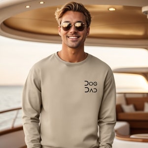 Pu&ograve; includere: Una felpa beige chiaro con una grafica nera che dice "DOG DAD" sul davanti.
