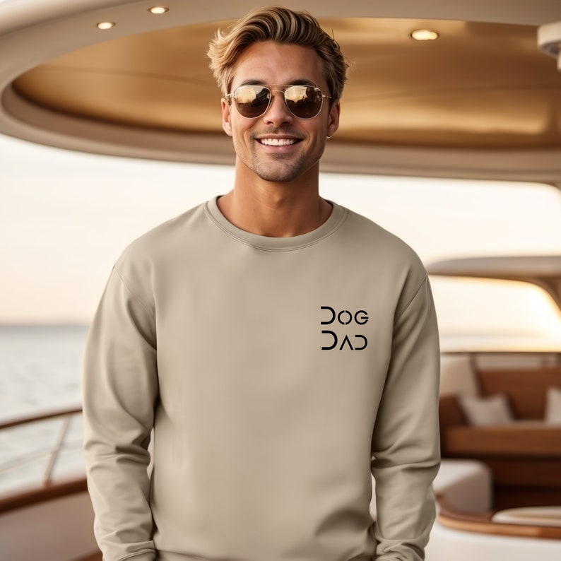 Pu&ograve; includere: Una felpa beige chiaro con una grafica nera che dice "DOG DAD" sul davanti.