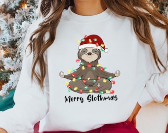 Peut inclure: Sweat-shirt blanc avec un paresseux de dessin animé méditant, orné de guirlandes lumineuses et d'un bonnet de Père Noël. Le texte "Merry Slothmas" est imprimé en dessous. Un article de fête pour les fêtes de fin d'année.