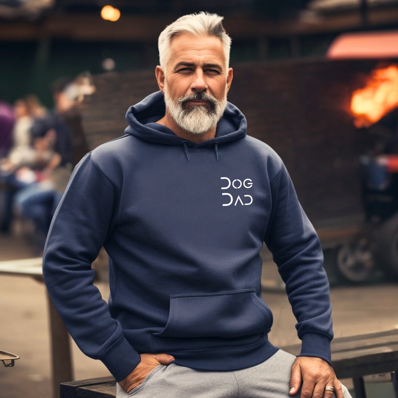 Pu&ograve; includere: Una felpa con cappuccio blu navy con una grafica bianca che recita "DOG DAD" in un font geometrico.