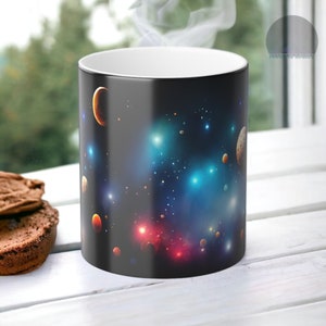 Puede incluir: Una taza de cerámica negra con un diseño de galaxia que presenta planetas, estrellas y nebulosas en tonos azules, rojos y naranjas.