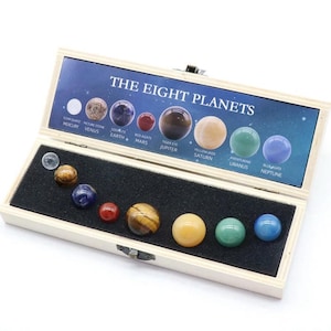 May include: A wooden box with a blue background and the words "The Eight Planets" printed on it. The box contains eight small, round, gemstone spheres representing the planets in our solar system. Each sphere is labeled with the name of the planet and the type of gemstone used.