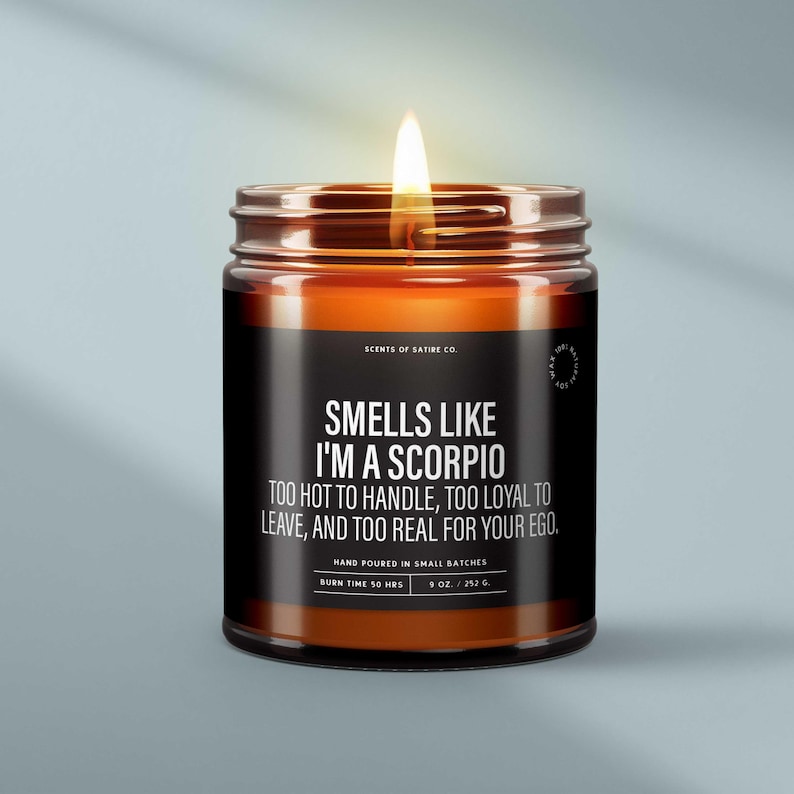 May include: A lit scented candle in a glass jar with a black label. The label reads "Smells Like I'm a Scorpio" with a humorous description. The candle is 3 inches tall and burns for 50 hours.
