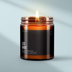 May include: A lit amber glass candle with a black label that reads "LEO BABY." The candle is labeled "Hand Poured in Small Batches" and "Burn Time 50 Hrs." It measures 9 oz / 252 g.