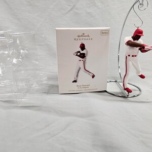 May include: Hallmark Keepsake Ornament Series featuring Ryan Howard of the Philadelphia Phillies in a red and white baseball uniform, swinging a bat. The ornament is on a silver stand.