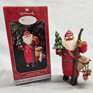 May include: A Hallmark Keepsake Ornament Club 1998 membership ornament featuring a red-clad Santa Claus carrying a small tree and a sack of gifts. The ornament is titled "Making His Way" and is part of the Folk Art Americana Collection.