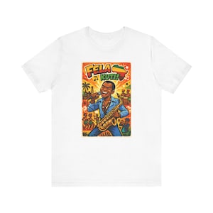 May include: White t-shirt featuring a colorful graphic of a musician playing a saxophone and singing into a microphone. The graphic includes the text "Fela Kuti!" and an image of the African continent. The musician is wearing a blue suit.