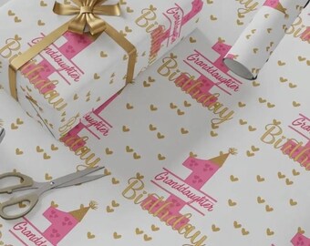 May include: White wrapping paper featuring a repeating pattern of pink number ones with gold party hats and the text Granddaughter Birthday in gold and pink script, with a gold ribbon bow on a wrapped box and a pair of metal scissors.