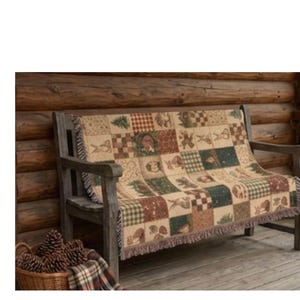 May include: A woven throw blanket featuring a patchwork design of squares with various nature-themed illustrations including pine trees, bears, rabbits, and checkered patterns in shades of green, brown, cream, and red with fringed edges.