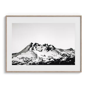 May include: A framed black and white print of a mountain range covered in snow. The artwork is in a light-colored wooden frame, with the mountain peaks and lower areas in dark tones against a white sky.