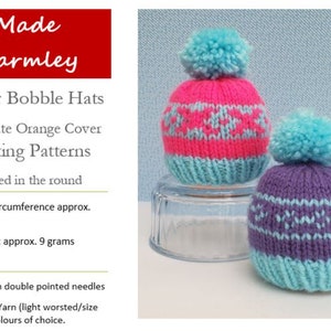 May include: Two small knitted bobble hats with light blue pom-poms. One hat is hot pink with light blue patterns, the other is purple with light blue patterns. Text reads: Made Warmley, Winter Bobble Hats, Chocolate Orange Cover Knitting Patterns, Knitted in the round, Size: to fit circumference approx. 20.5cm, Item weight: approx. 9 grams, Set of 3.5mm double pointed needles, Double Knit Yarn.