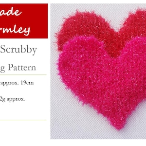 May include: Two pink heart-shaped knitted scrubbies, one slightly larger than the other, with a fuzzy texture. The scrubbies are made with a sparkly yarn. The image includes text: "Made Warmley Heart Scrubby Knitting Pattern Heart at widest approx. 19cm Heart weight: 12g approx. 5mm needles Tapestry needle"