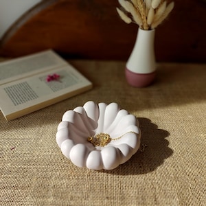 Peut inclure: Plat en céramique blanche avec un bord festonné, en forme de fleur, contenant un collier en chaîne dorée.