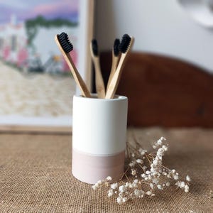 Peut inclure: Un porte-brosses à dents en céramique blanc et rose avec quatre brosses à dents en bambou aux poils noirs.