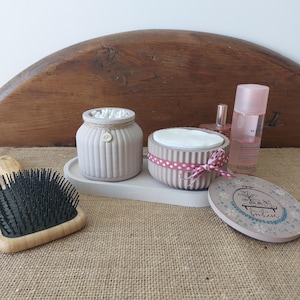 Peut inclure: Deux contenants en céramique avec couvercles, l'un rempli de cotons-tiges et l'autre de disques de coton. Les contenants sont de couleur rose clair avec une texture côtelée et un ruban à pois blancs autour du couvercle. Les contenants sont posés sur un plateau en bois avec un motif floral et les mots "Bonjour" et "Paris" sur le couvercle.