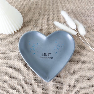 Peut inclure: Un plat en forme de cœur gris avec un motif bleu et blanc. Le plat porte l'inscription "ENJOY the little things".