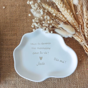 Op de afbeelding: Een wit, wolkvormig keramieken schaaltje met de Franse tekst 'Veux-tu devenir ma marraine pour la vie?', een klein hartje, de naam 'Jade' en de tekst 'Dis oui!' gedrukt in een lichtgrijs, schreefloos lettertype.