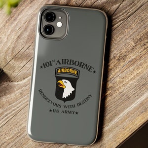 May include: A gray phone case with a black and white 101st Airborne emblem. The emblem features a white eagle with a yellow beak and yellow lettering that reads "AIRBORNE". The text around the emblem reads "*101st AIRBORNE*  RENDEZVOUS WITH DESTINY *US ARMY*"