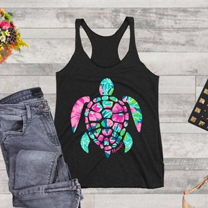 May include: Black tank top with a floral patterned sea turtle graphic and the word "Hawaii" underneath. The tank top is on a wood background with a pair of jeans, a purse, and a pair of high heels.