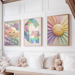 Puede incluir: Tres impresiones artísticas enmarcadas con temática infantil. Una presenta una nube sonriente, otra una colorida letra "G" con el nombre "Gabriela" y la tercera un sol sonriente. Las impresiones se exhiben sobre un banco empotrado con almohadas y peluches.