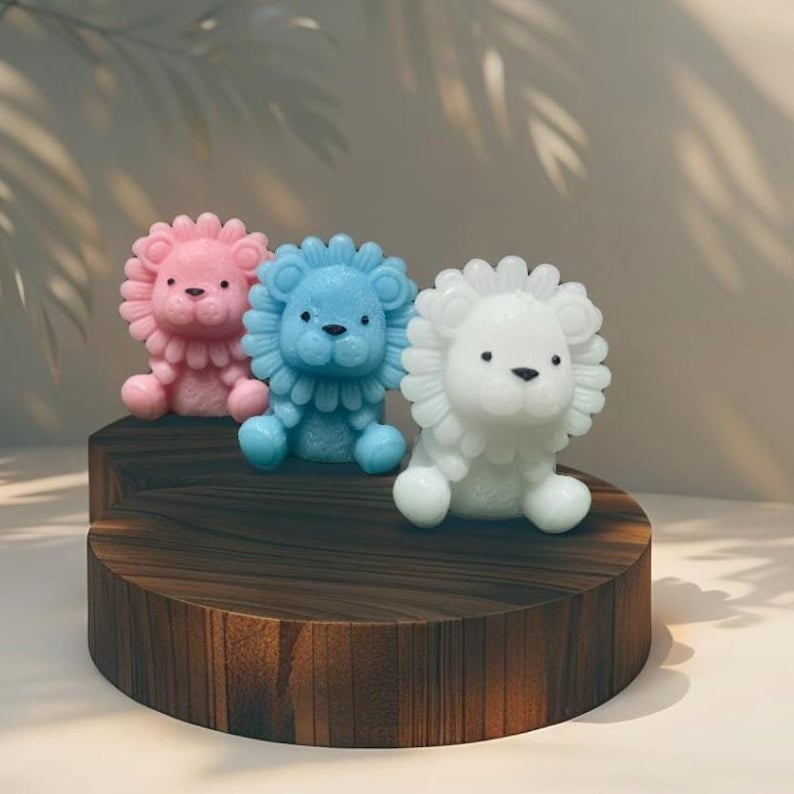 May include: Three colorful lion figurines in pink, blue, and white sit on a dark wooden display. The lion figures have detailed manes and sweet facial features. The background is a soft, neutral color.