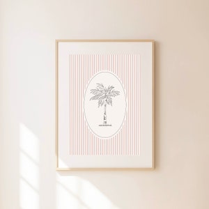 May include: Framed art print featuring a black line drawing of a palm tree within an oval frame. The background has vertical red stripes. The artwork is encased in a light-colored wooden frame, suitable for wall decor.