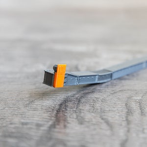Puede incluir: Una vía de tren modelo gris con una luz de señal naranja al final.