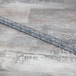 Puede incluir: Un modelo de puente de metal plateado con un diseño de celosía. El puente está hecho de finas barras de metal que se conectan para formar una serie de triángulos.