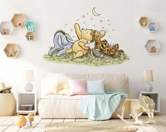 Puede incluir: Una calcomanía de pared de Winnie the Pooh con Winnie the Pooh, Piglet, Tigger y Eeyore mirando hacia arriba a una luna creciente y estrellas. La calcomanía está en una pared blanca en una guardería con un sofá blanco, una lámpara y un caballo de balancín.