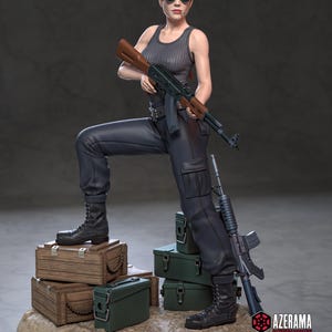 Pode incluir: Uma figura de uma mulher em um top preto, calças e botas, segurando um rifle. Ela está em pé sobre caixas de madeira e caixas verdes. Um segundo rifle está encostado nas caixas. A figura está usando óculos de sol e tem cabelo curto ruivo.